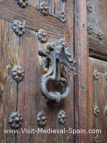 Close up photo of a studded wooden door showing the metal door knocker in the shape of a dragon.
